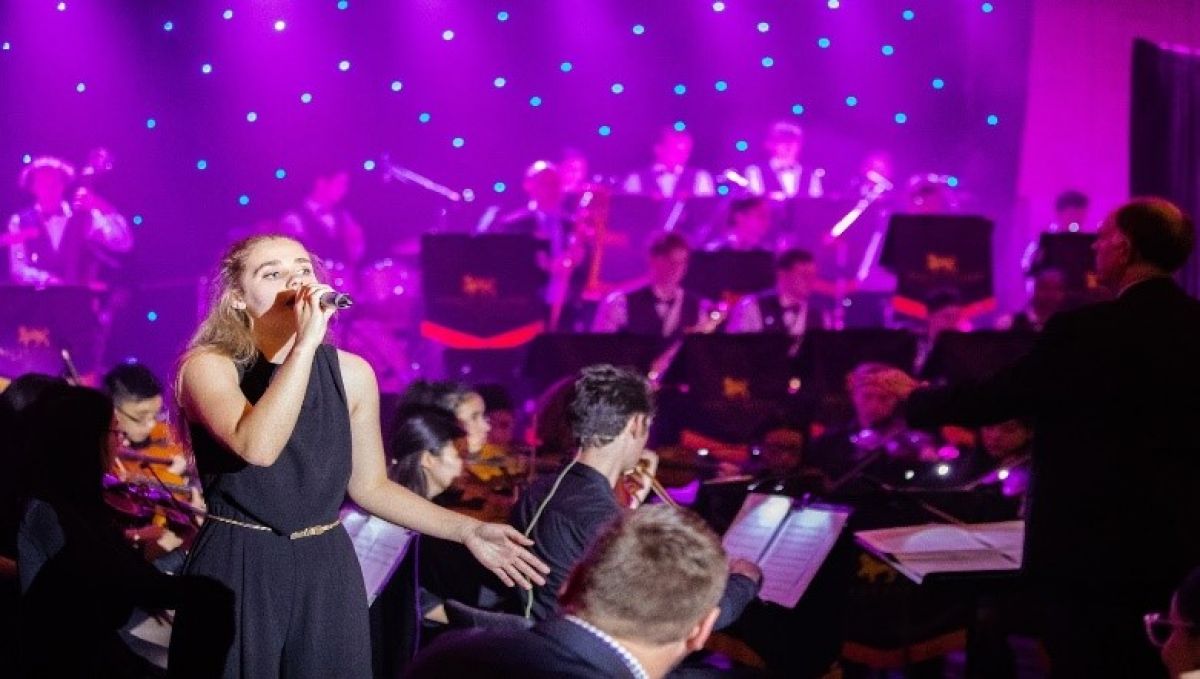 A Wesley student singing in front of a Jazz band and conductor