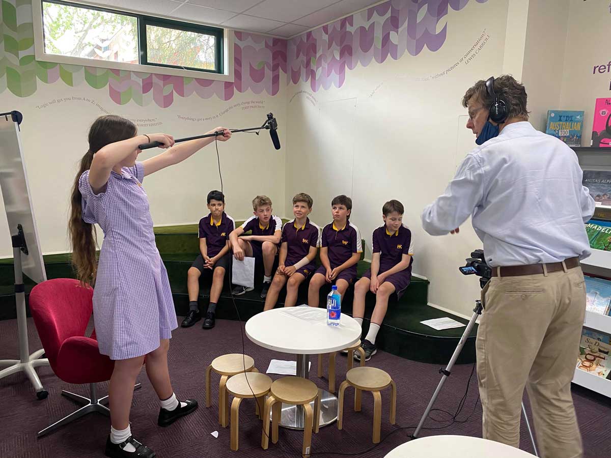 Five students sit on a couch and are interviewed by another student who holds a boom mic