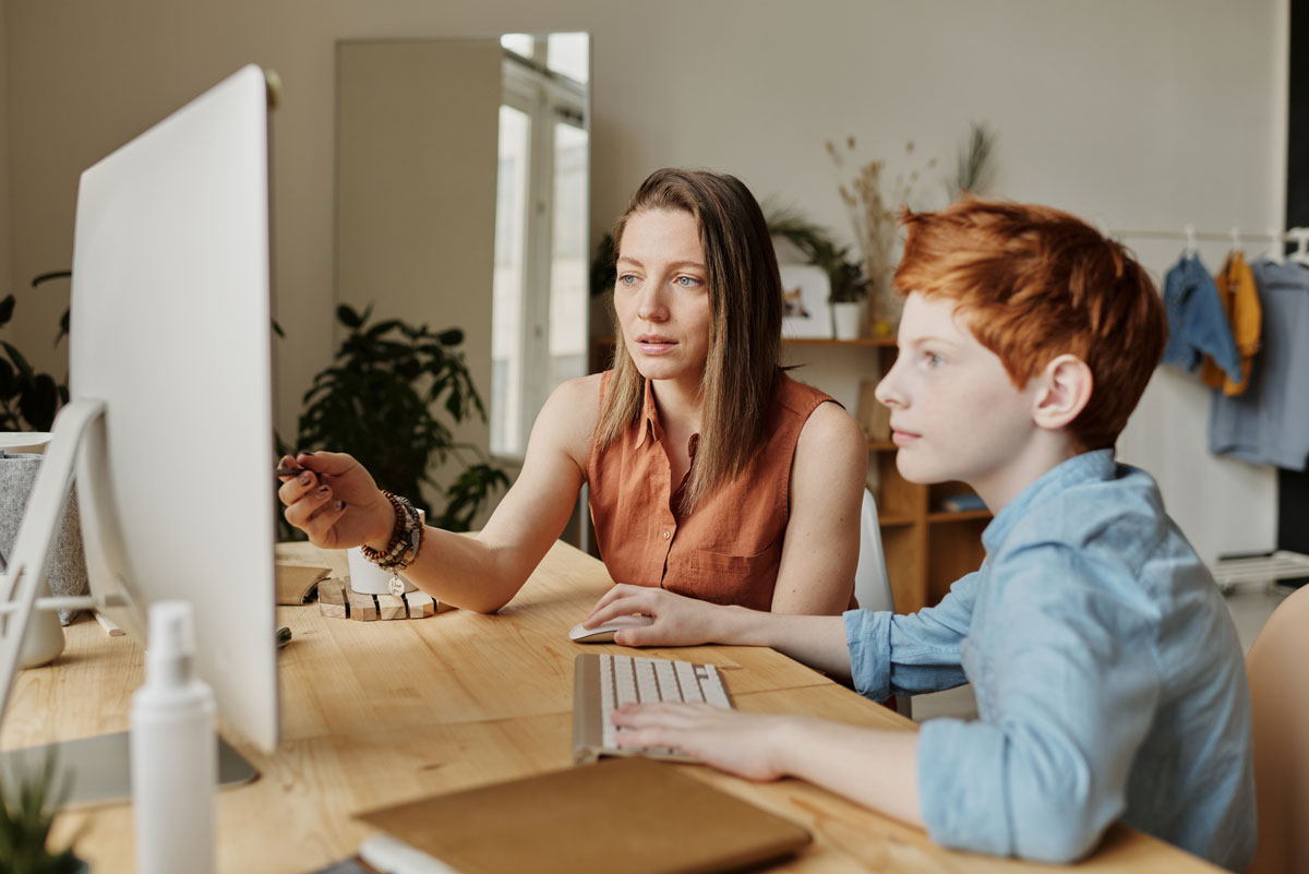 A mother teaches her son at home, and they look at a computer together