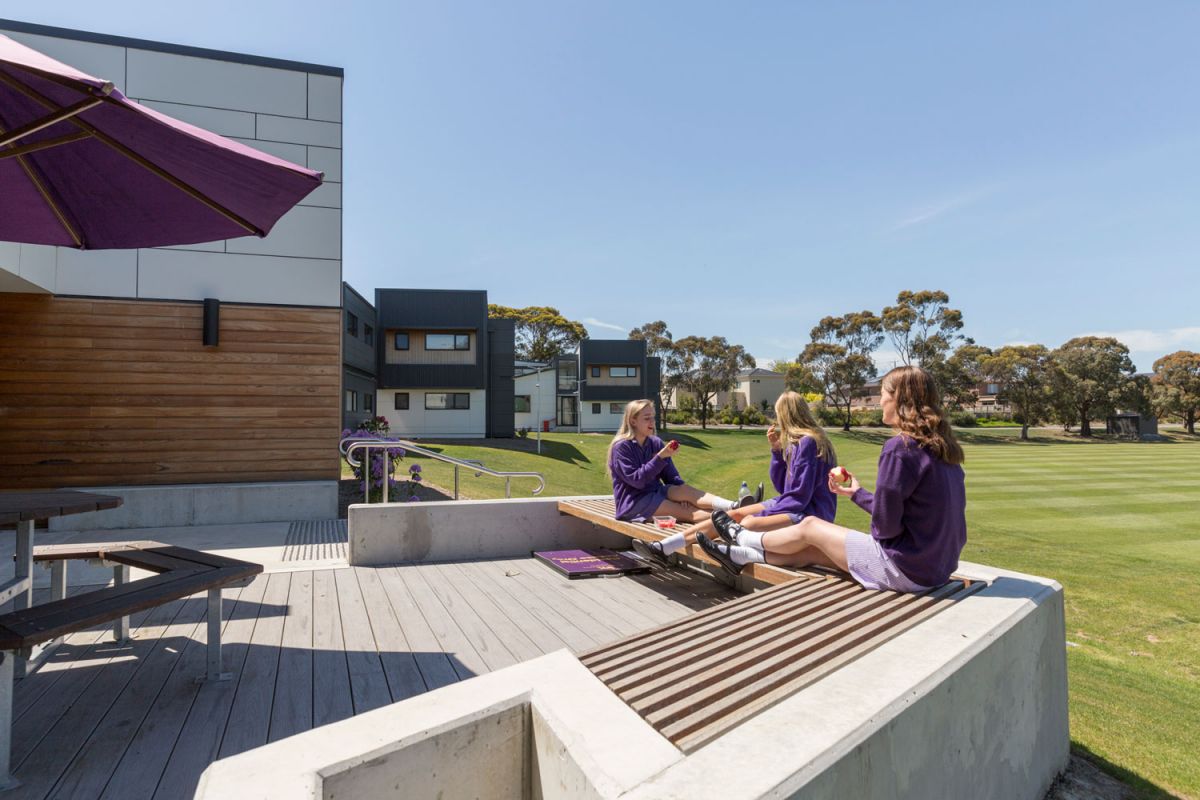 Three girls sitting on the edge of a terrace overlooking a field