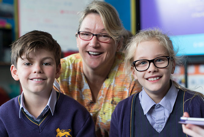 A teacher and two young students in class smiling to camera