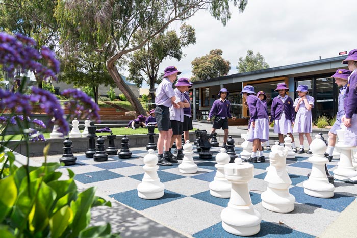 Young children in school uniform playing on a giant chessboard