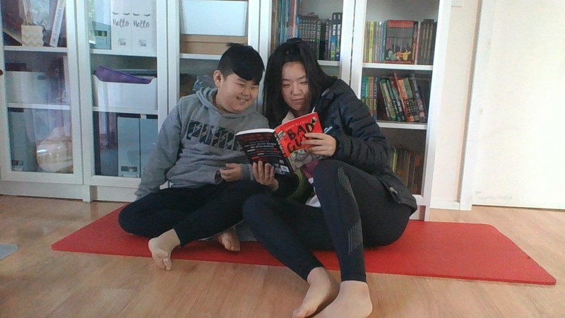 Two siblings read a book together on the floor of their house