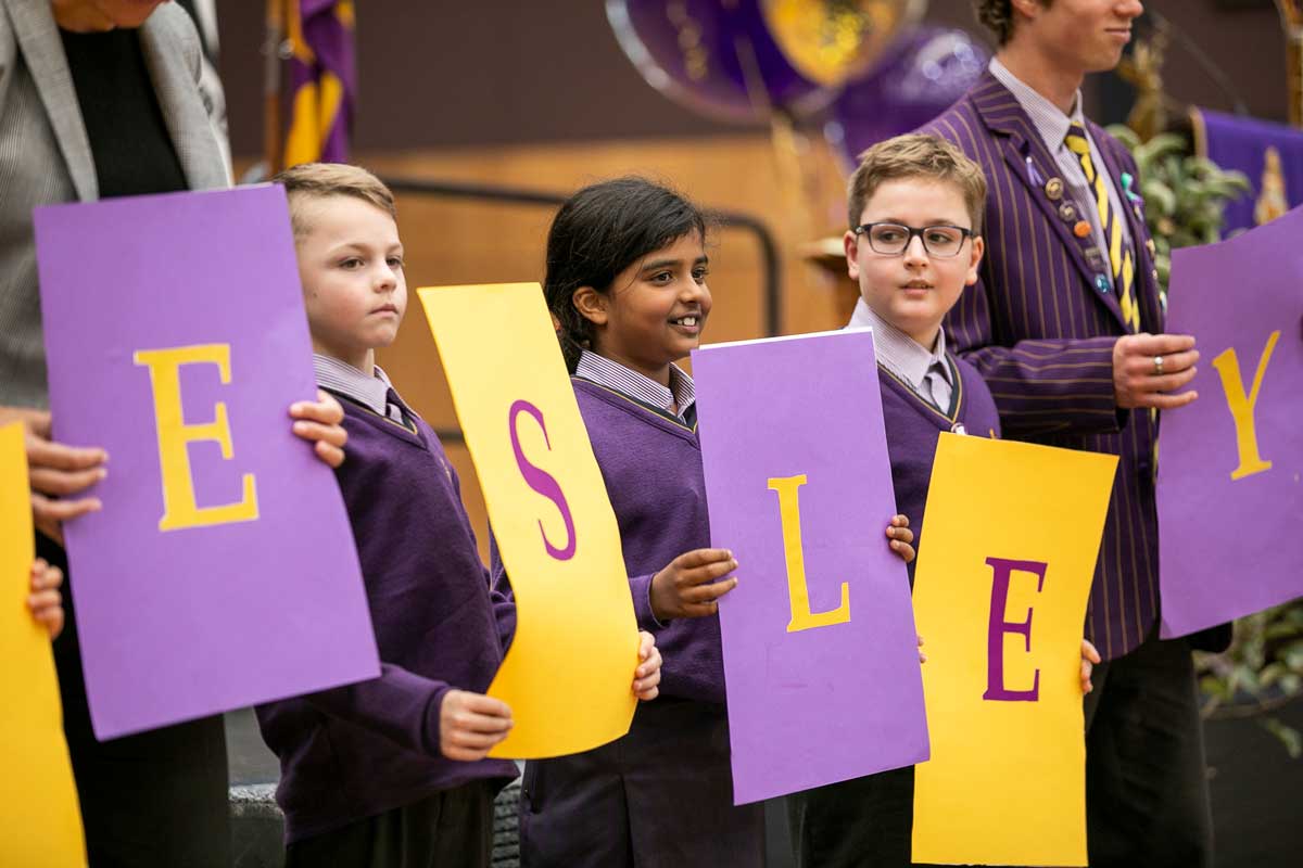 Children hold up signs with letters for the word WESLEY