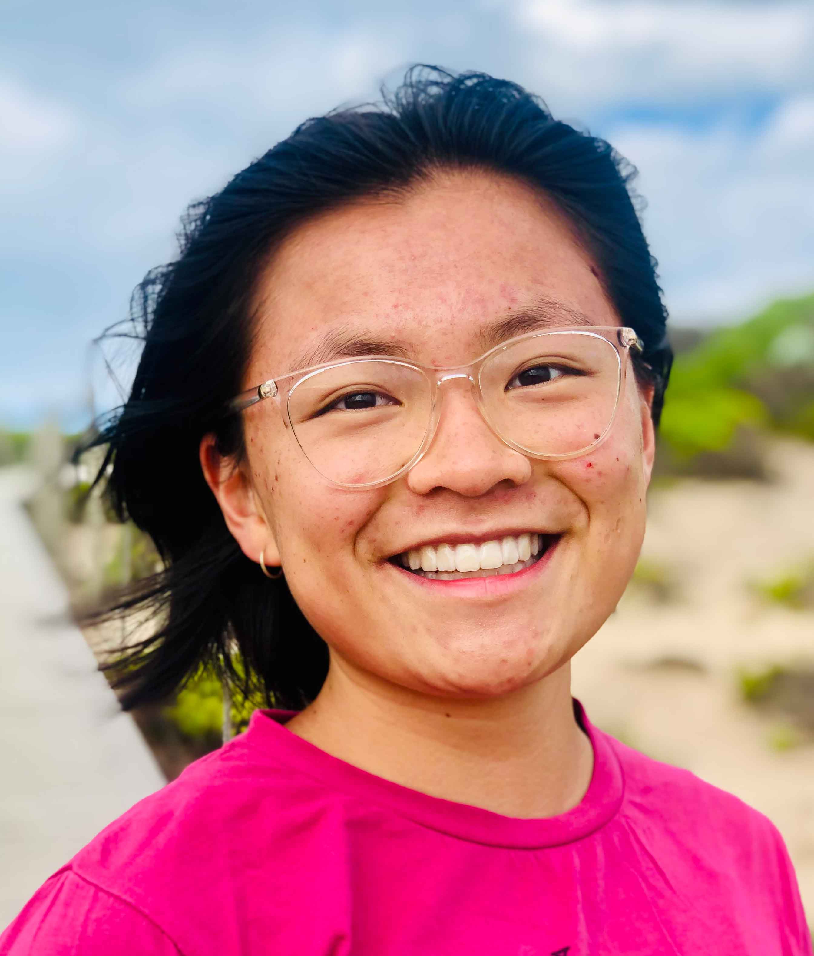 Headshot of Grace Danielson in pink t-shirt and the beach in the background