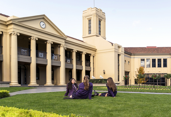 Three female students sitting on the grass at the front of St Kilda Road Campus