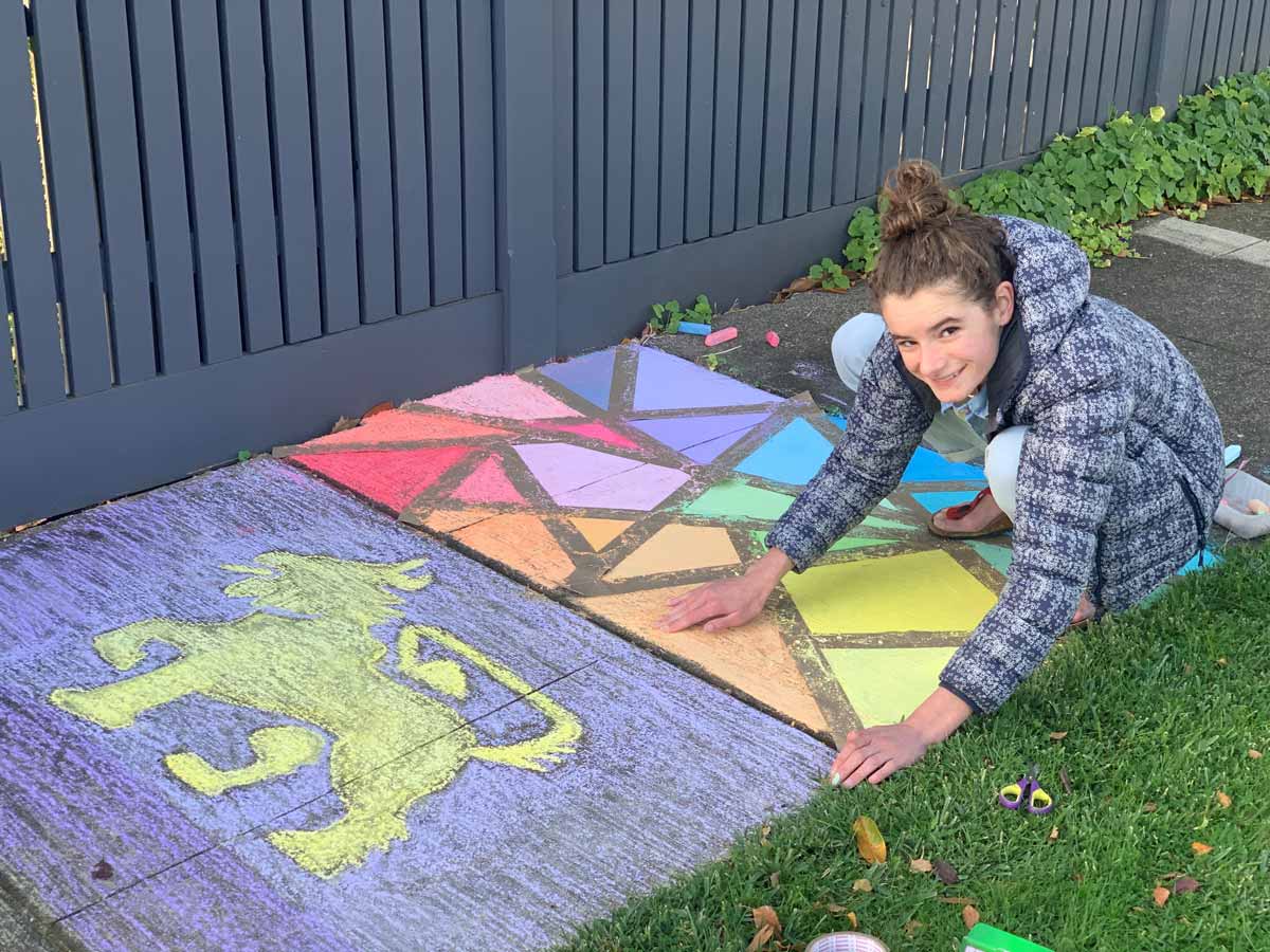 A girl draws graphics on the footpath with coloured chalks