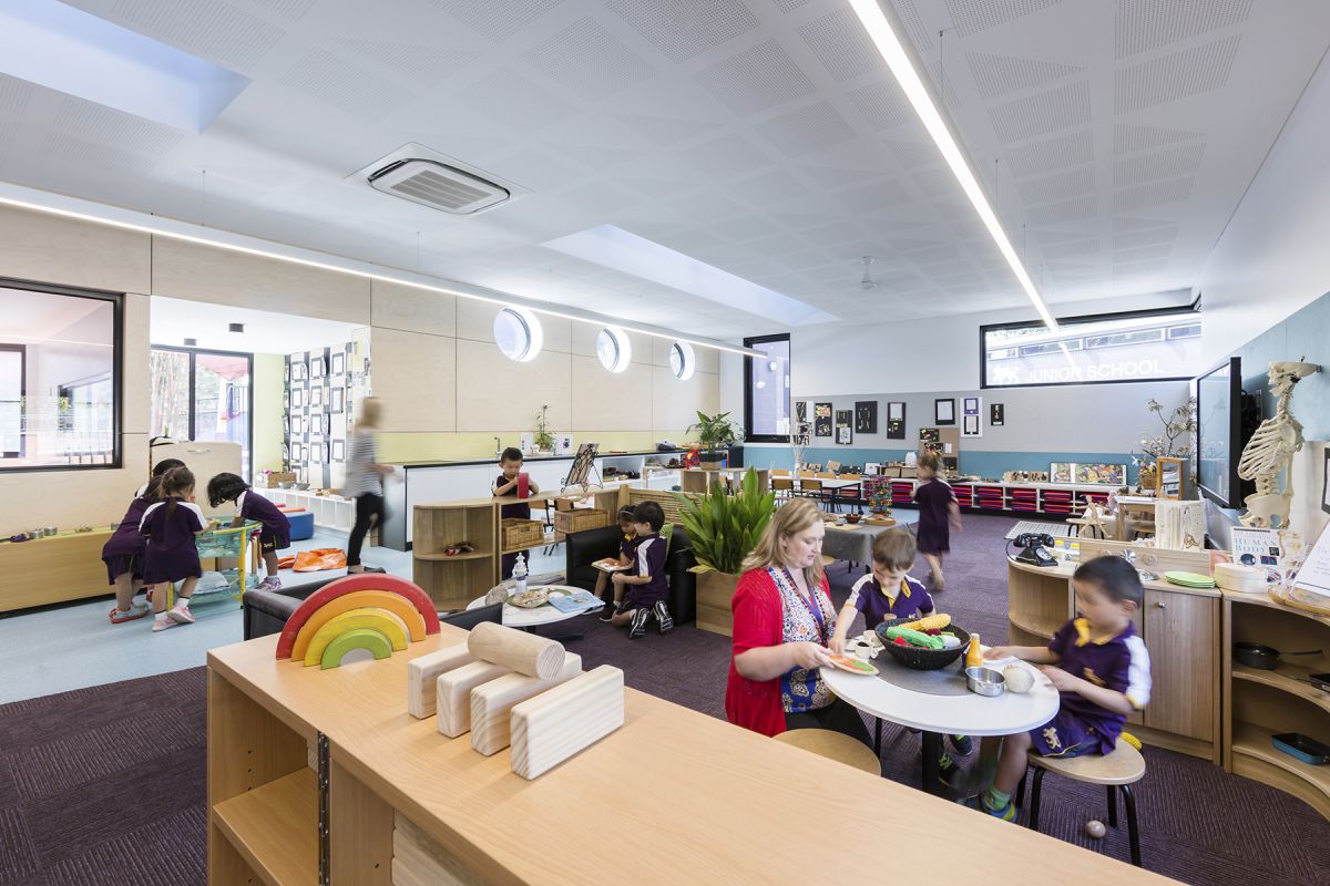 Children and teachers seated at different tables in a large classroom