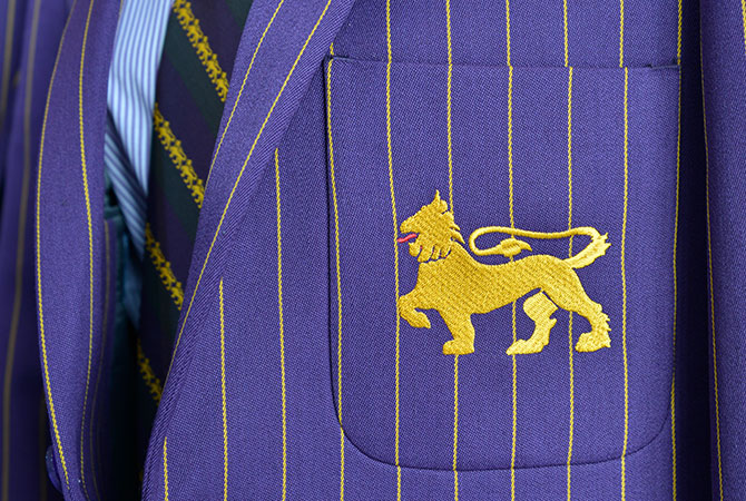 Close up of a gold embroidered lion on the pocket of a purple blazer