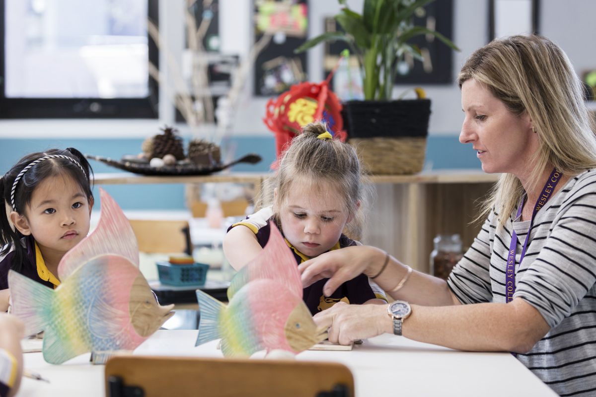 A teacher showing two children arts and craft at a table