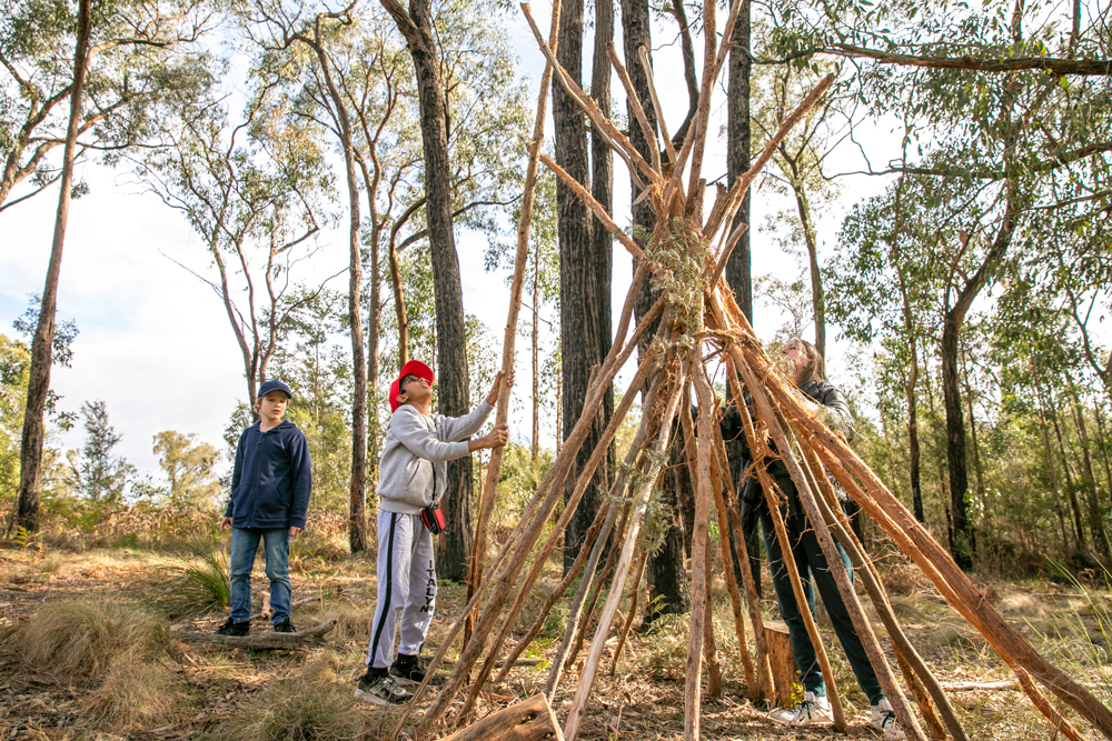 Students building wood teepee structure at outdoor education camp site