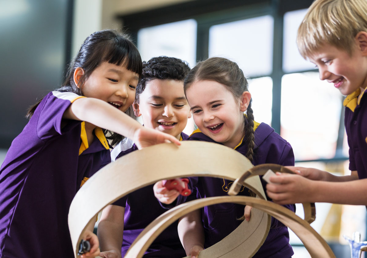 Four students play with a circular wooden toy