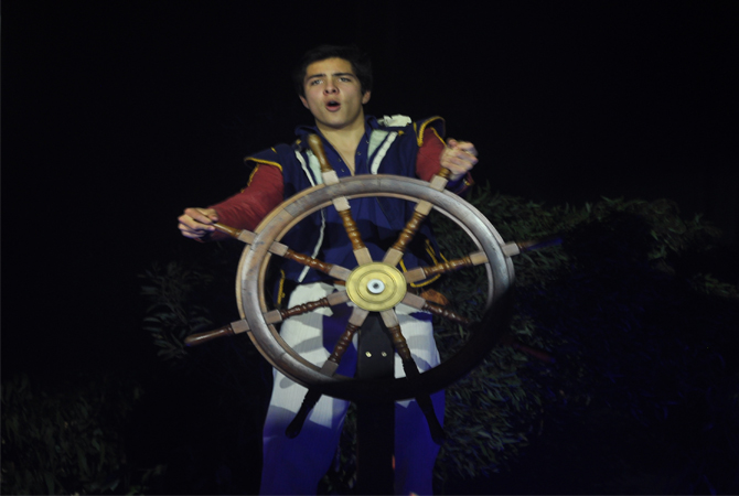 Student dressed in a ship captain's costume at a ship wheel in the stageplay The Tempest