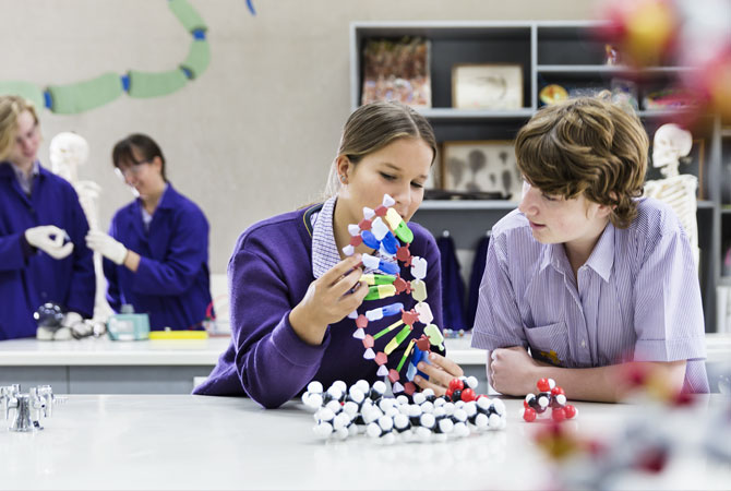 Middle school girl and boy in science lab examining a model of DNA