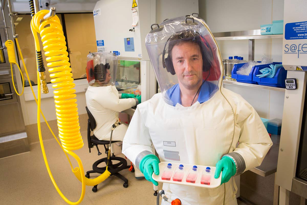 Dr Julian Druce in a hazmat suit holding samples