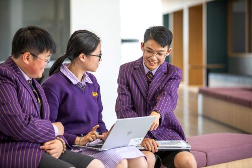 Three students sitting on a couch, looking at a laptop