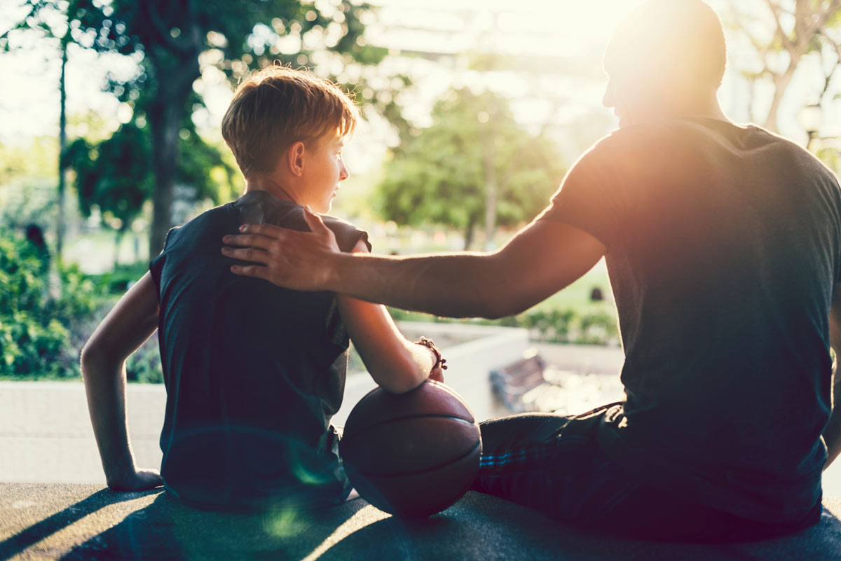 Silhouette of father and son with basketball beside them