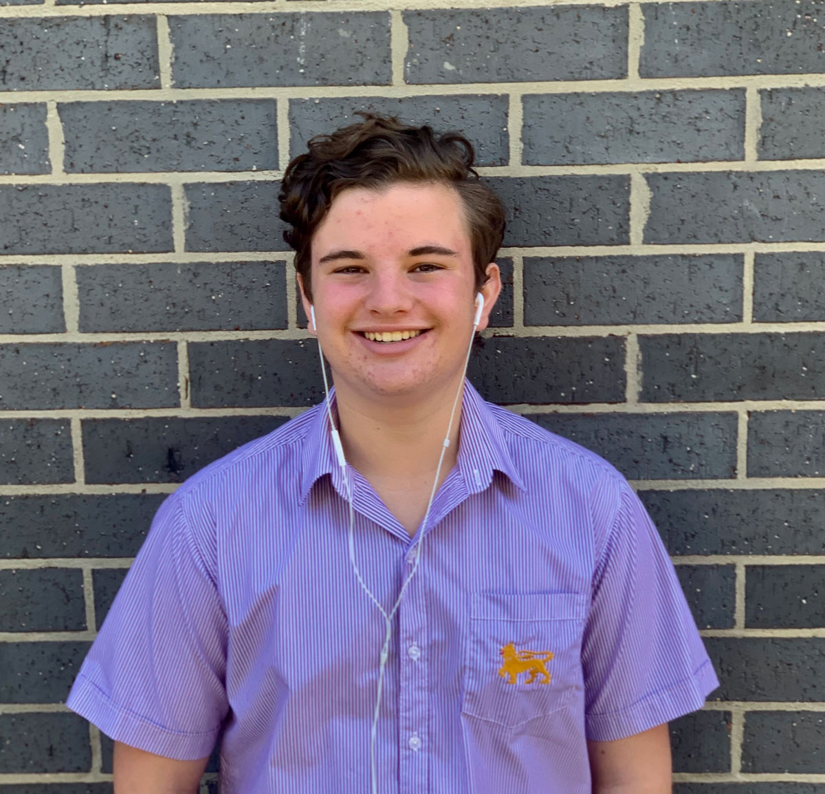 Cody Brits stands in front of a brick wall in his Wesley uniform shirt and with headphones in