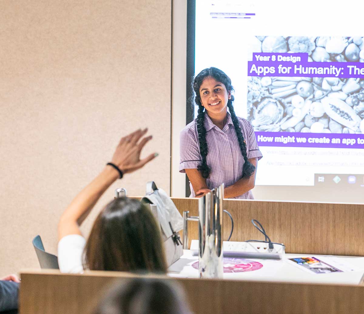 A student stands in front of the board, which has a projected image saying Year 8 Apps for Humanity Showcase